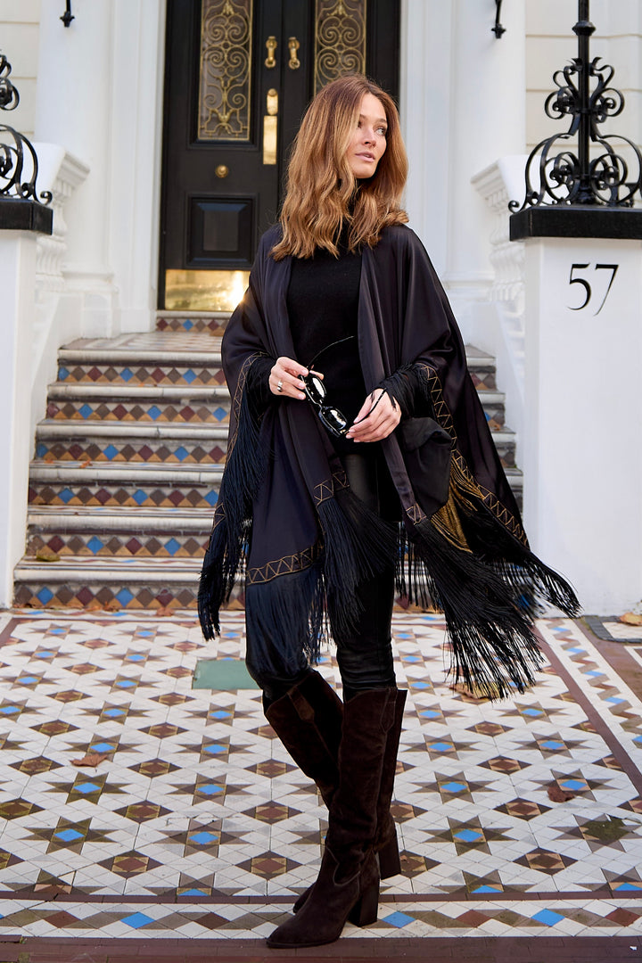 The Nomad Poncho in black silk with gold hand embroidery and black fringe, side view, London townhouse steps