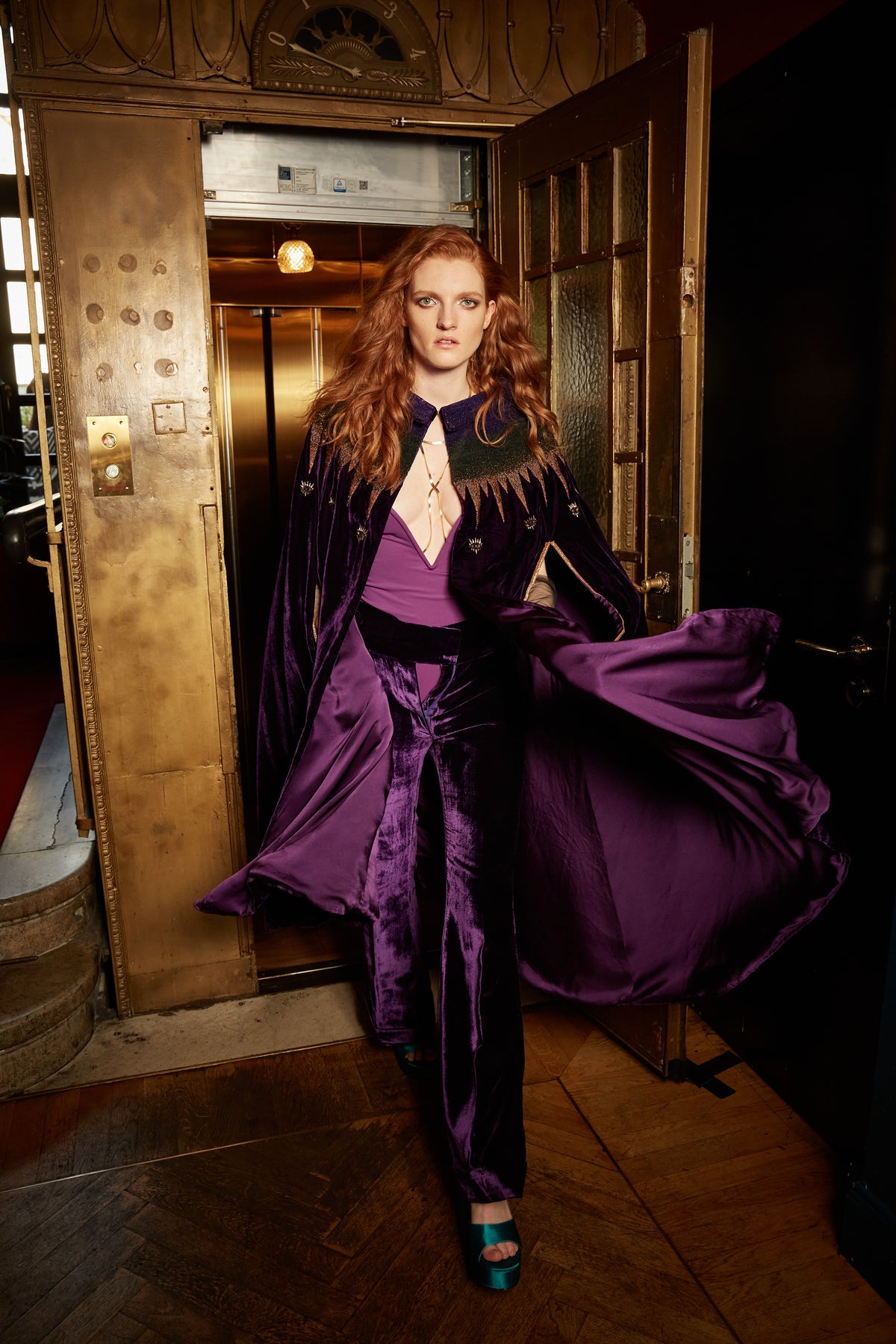 The Rainbow Cape in purple silk velvet with rainbow sequin collar, in motion, hotel lift