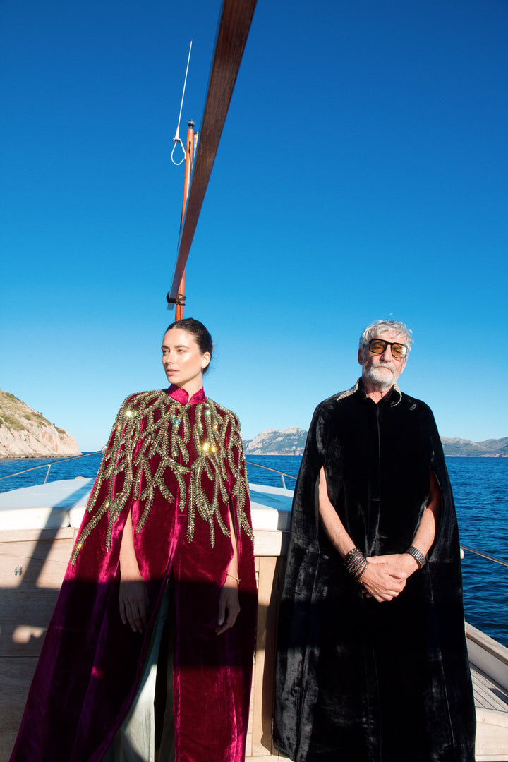 The Royal Garden Cape in magenta silk velvet with gold and green leaf embroidery, on the deck of a sailing boat