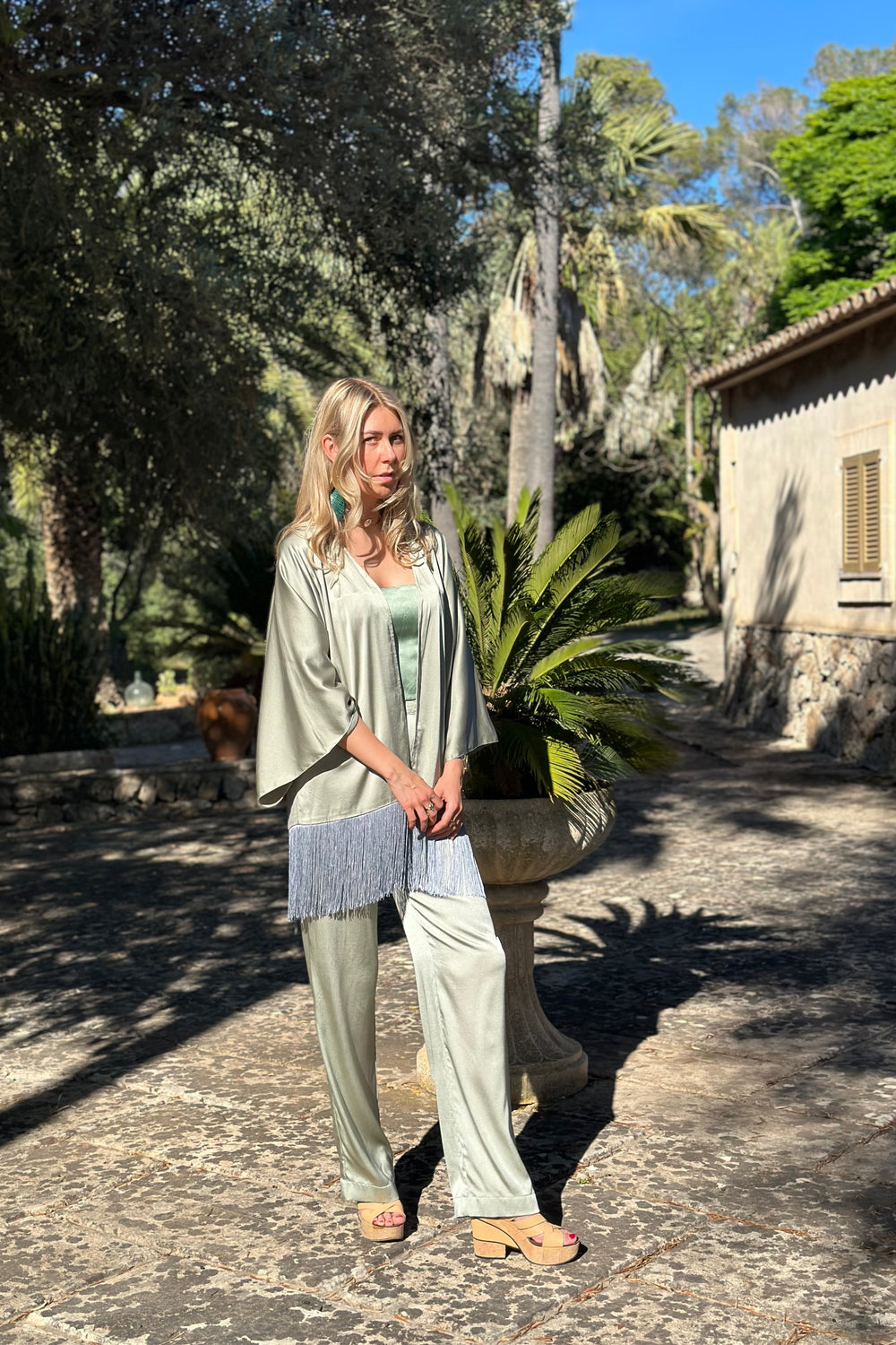 The Sage Leaf Kimono in sage green silk with fringe, front view with matching trousers, garden