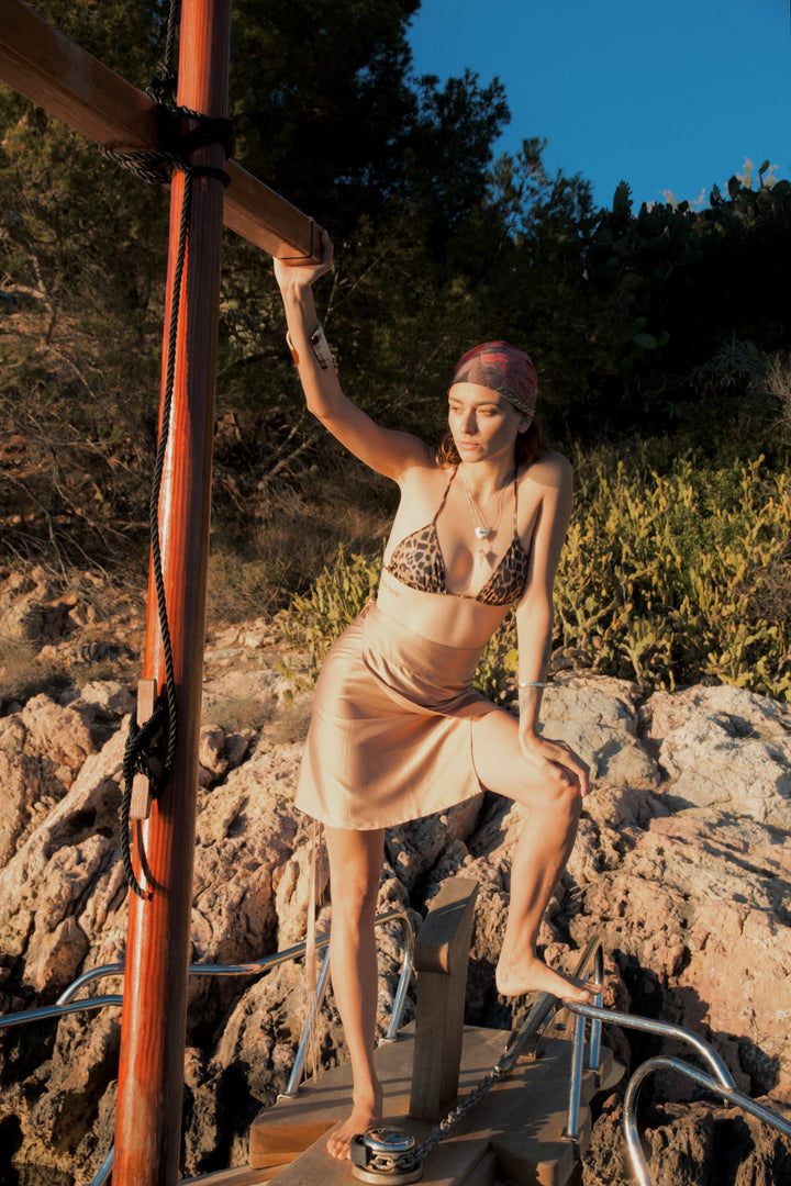 The Sand Wrap Skirt in sand silk, on a sailing boat by rocks