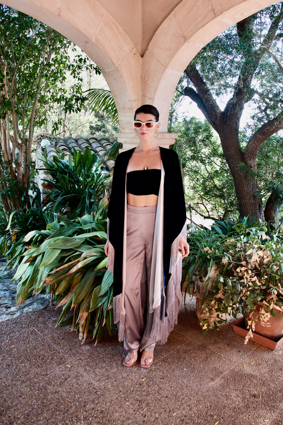 The Silver Grey Trousers in silver grey silk, styled with a black velvet poncho, garden archway
