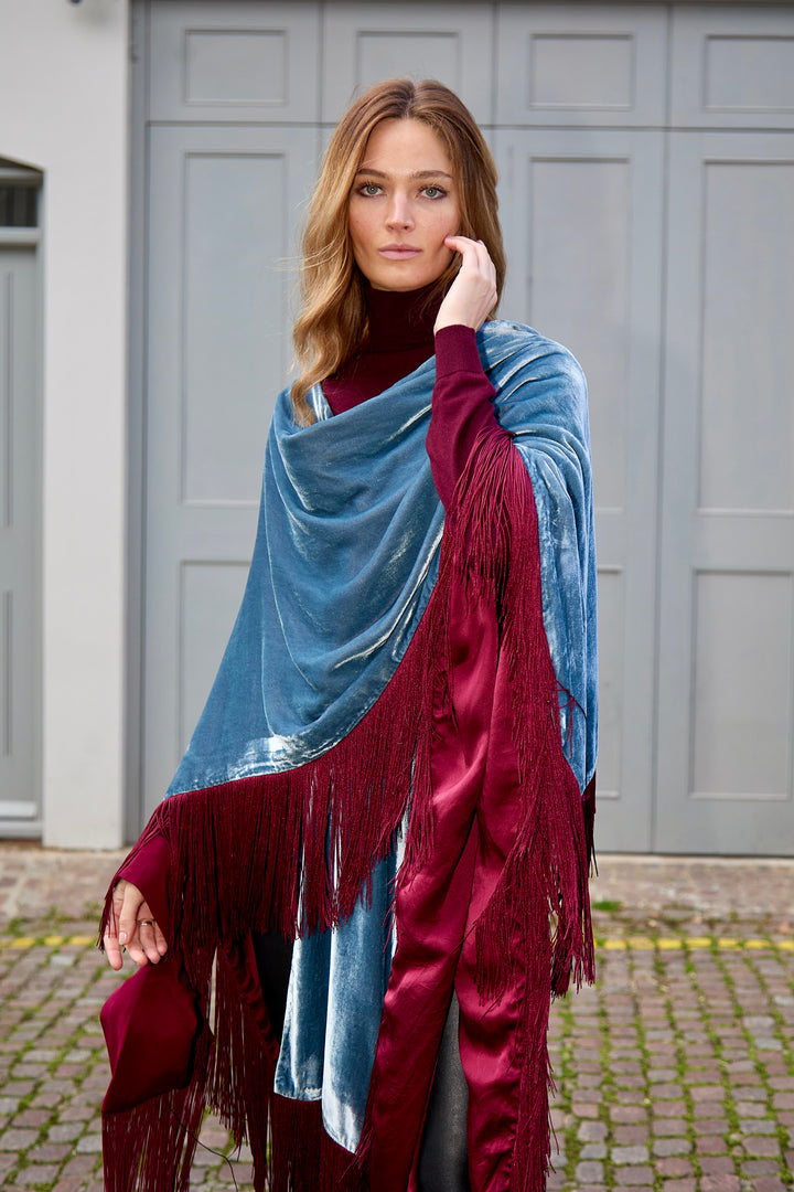 The Summer Cloud Poncho in pale blue silk velvet with burgundy fringe, front view, mews doorway