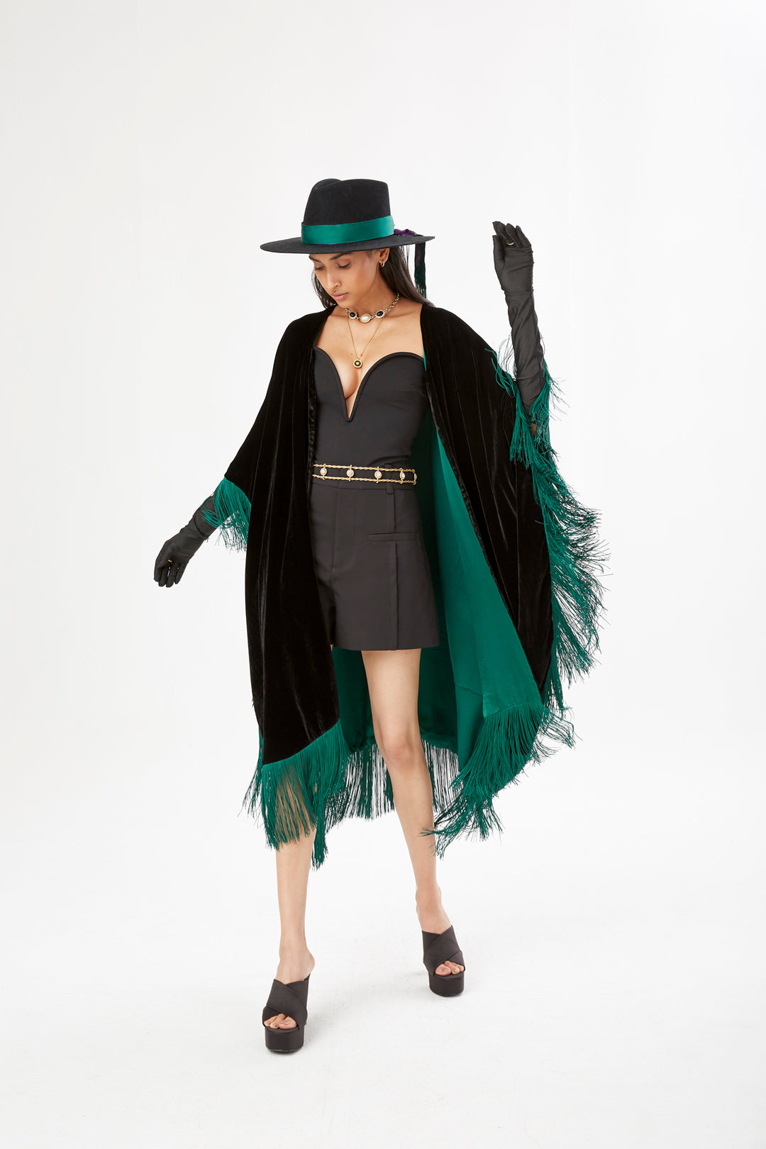 The Gypset Poncho in black silk velvet with emerald fringe, front view styled with a black hat, studio