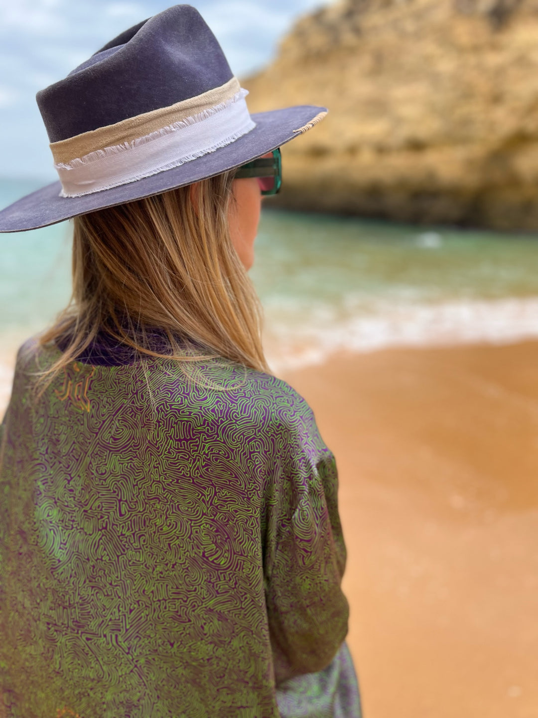 The Mazestroom Kimono, Purple and Green, in iridescent green and purple maze-print silk with velvet trim, back view, beach
