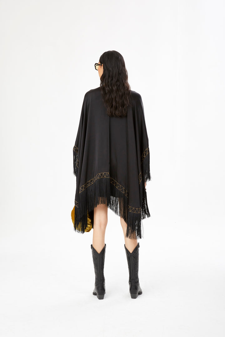 The Nomad Poncho in black silk with gold hand embroidery and black fringe, back view, studio