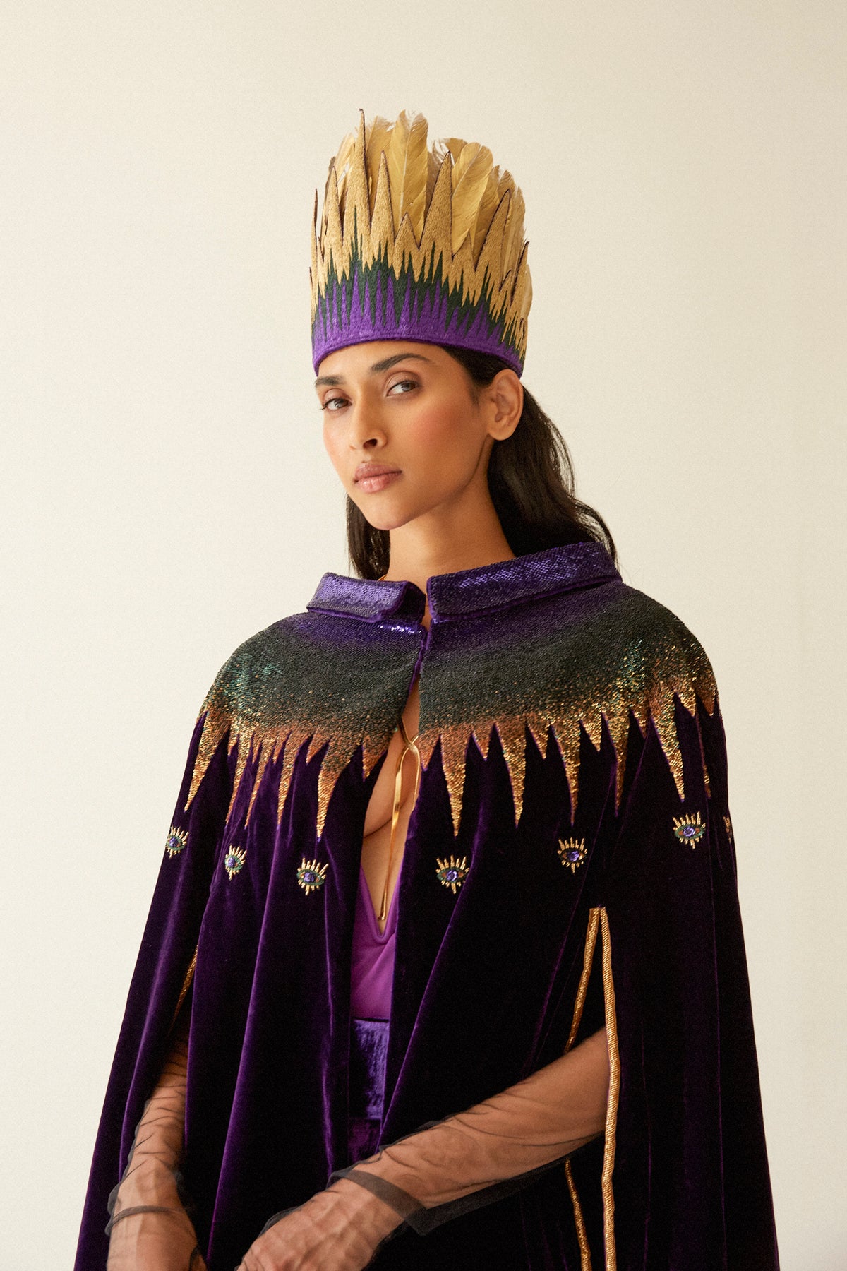 The Rainbow Feather Headdress with golden feathers on a purple band, styled with the Rainbow Cape, front view, studio